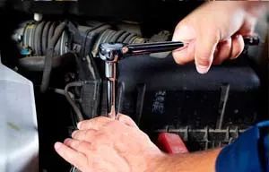 Un hombre está trabajando en el motor de un automóvil con una llave inglesa.