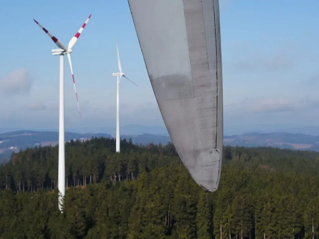 Tres aerogeneradores en la cima de una colina con árboles al fondo