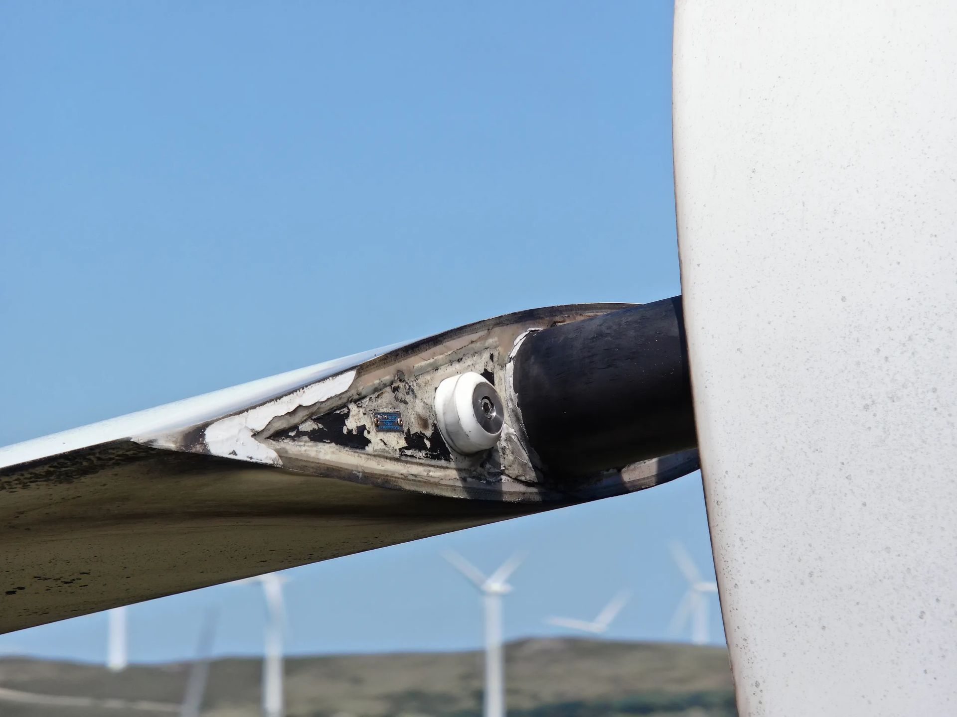 Un primer plano del ala de un avión con turbinas eólicas al fondo.