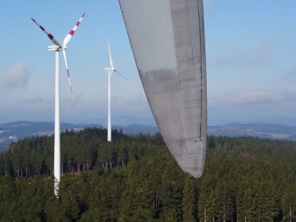Tres aerogeneradores en la cima de una colina con árboles al fondo