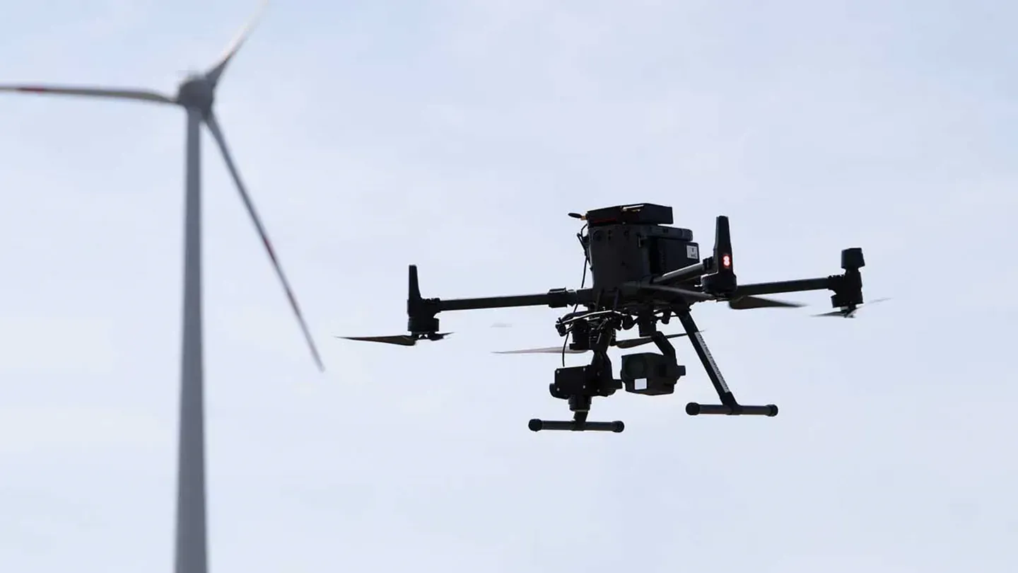 Un dron vuela delante de una turbina eólica.