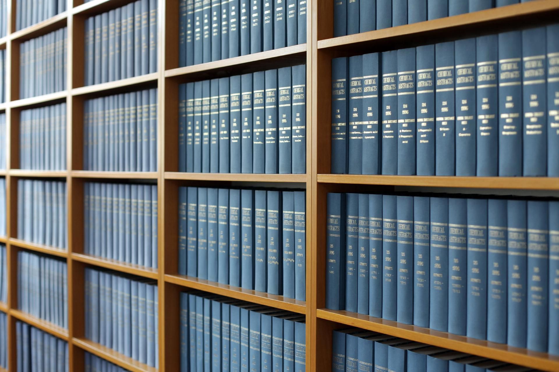 In einer Bibliotheksumgebung stehen Reihen identischer blauer, gebundener Bücher in Holzregalen.