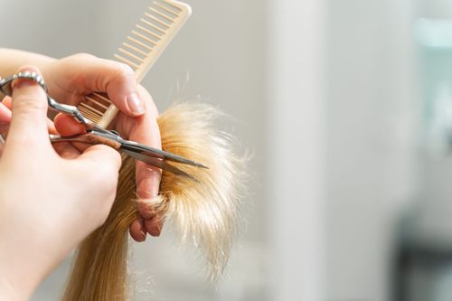 Ein Friseur glättet das braune Haar einer Kundin in einem Salon mit einem Glätteisen. Die Kundin sitzt auf einem Stuhl.