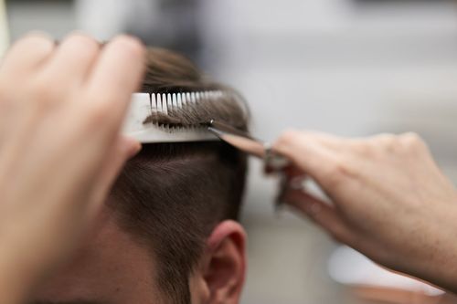 Ein Friseur schneidet einem Mann mit einer elektrischen Haarschneidemaschine einen Fade-Haarschnitt. Drinnen.