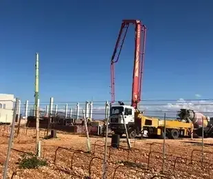 Un camión bomba de hormigón está bombeando hormigón a un viñedo.