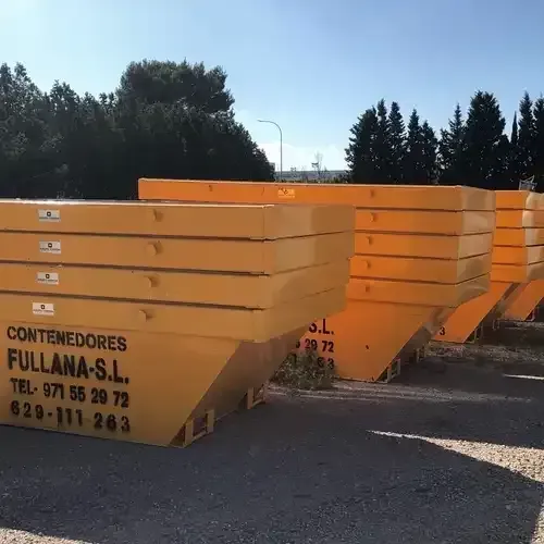 Una fila de contenedores de basura amarillos están apilados uno encima del otro en un estacionamiento.