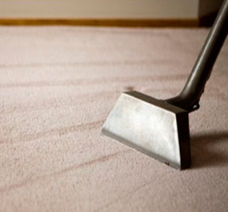 Una aspiradora está limpiando una alfombra rosa en una habitación.