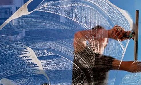 Un hombre está limpiando una ventana con una escobilla de goma.