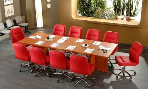 Una sala de conferencias con una mesa larga y sillas rojas.