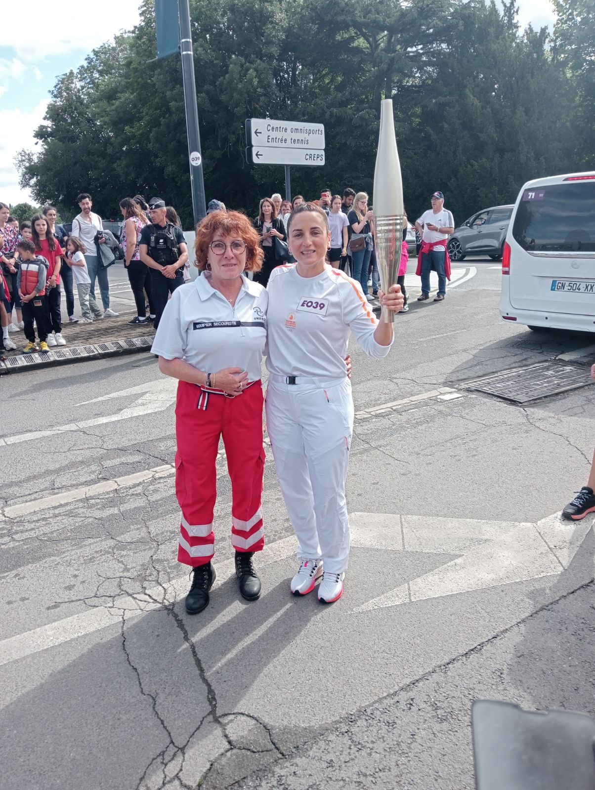 Jeune femme en blanc tenant la flamme olympique à côté d'une secouriste en rouge