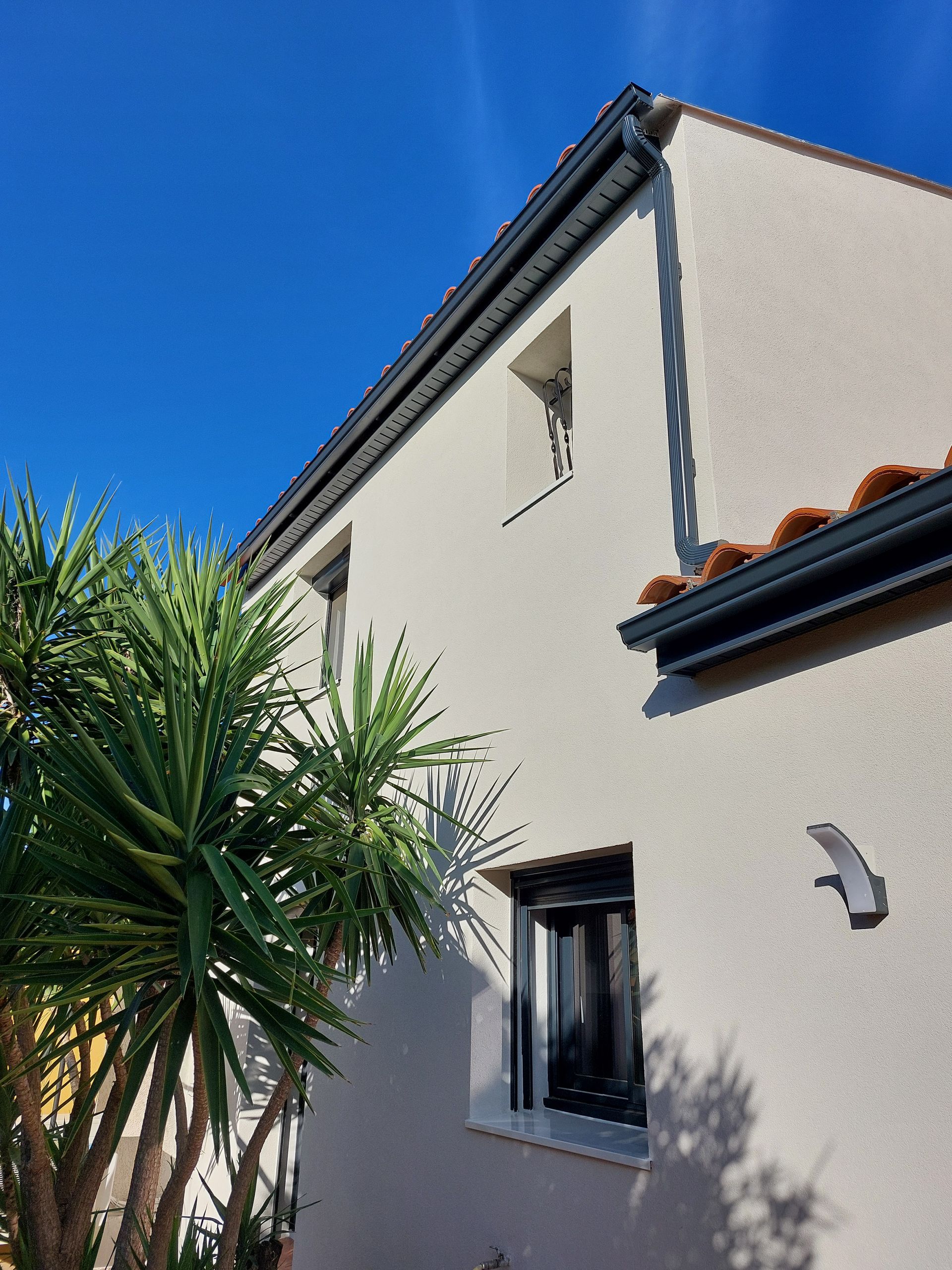 Maison en stuc blanc avec des boiseries bleues et un toit de tuiles rouges