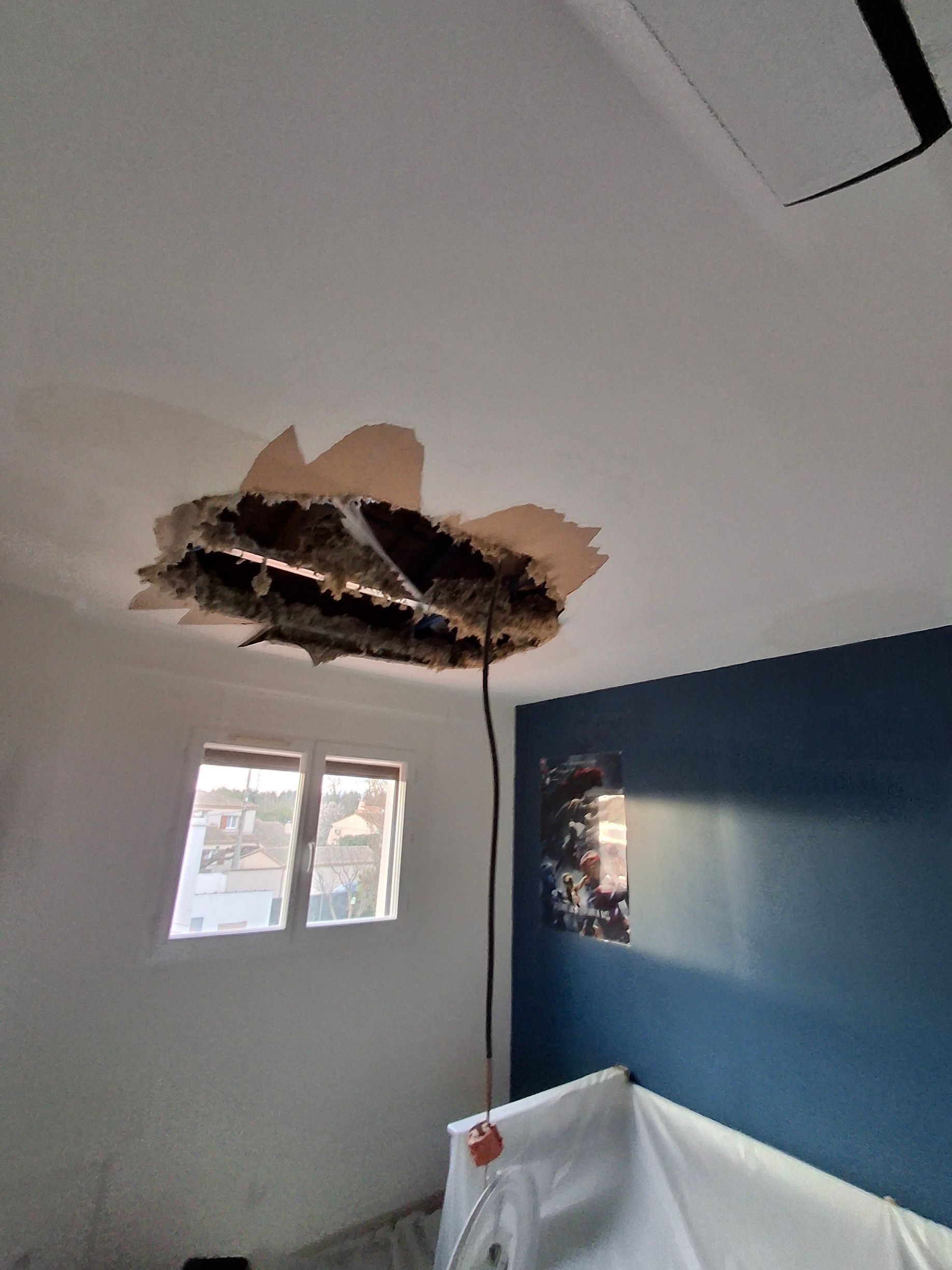 Trou au plafond et dégâts apparents dans une chambre, au-dessus d'un lit et d'un mur bleu.