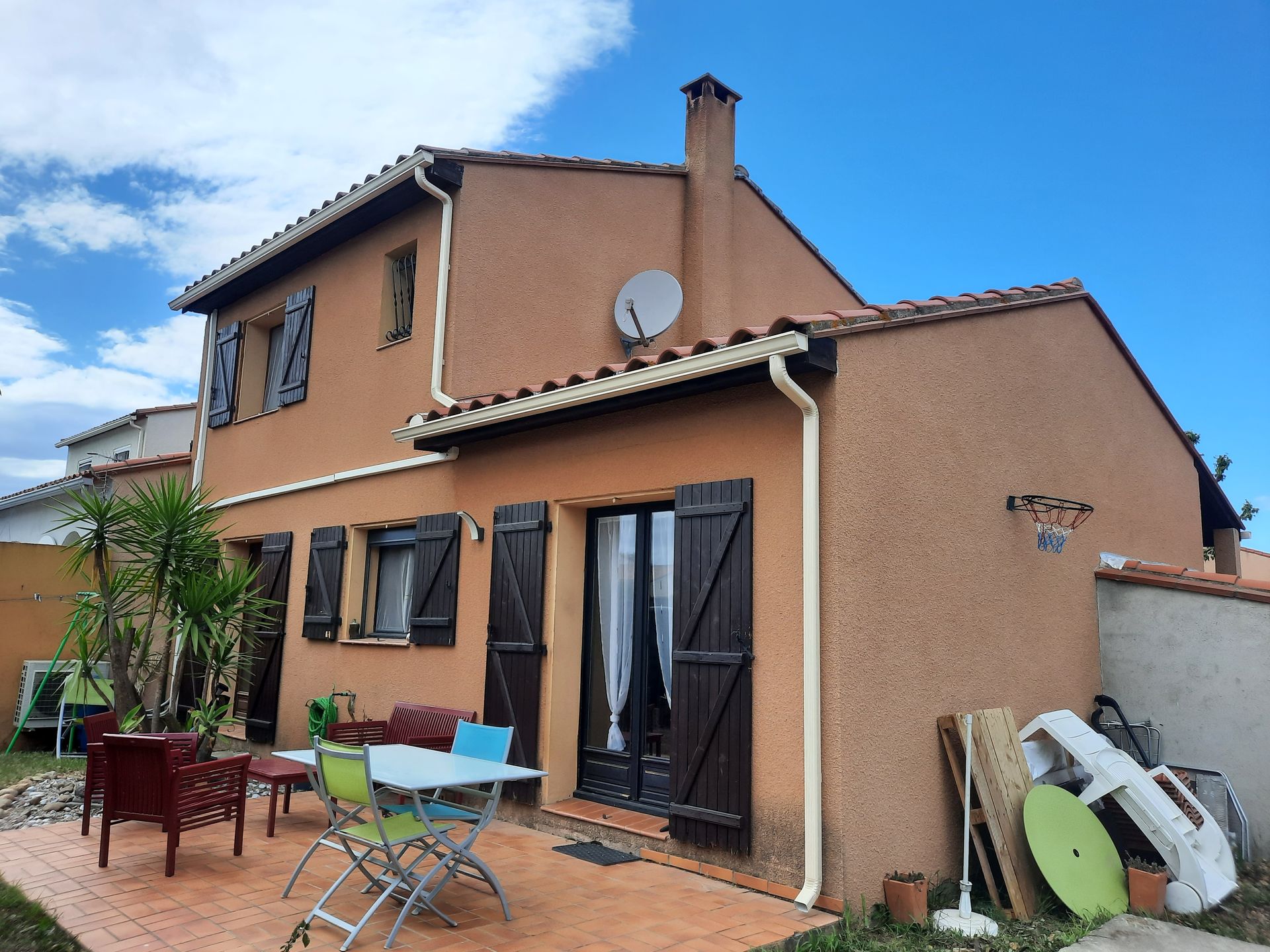 Maison à deux étages avec mobilier de patio et antenne parabolique par une journée ensoleillée
