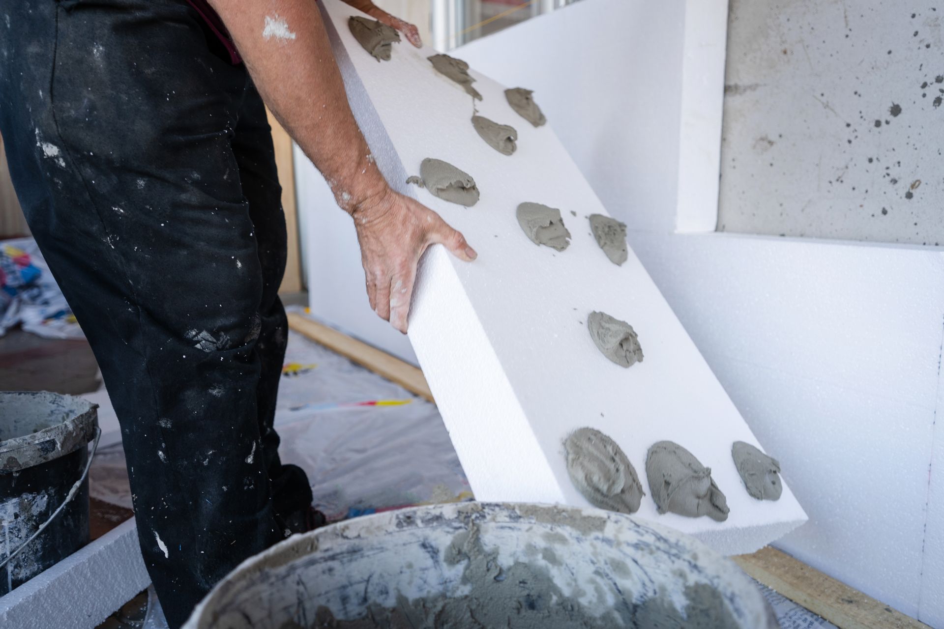 Un ouvrier applique des points de colle sur un panneau isolant blanc avant de le fixer au mur.