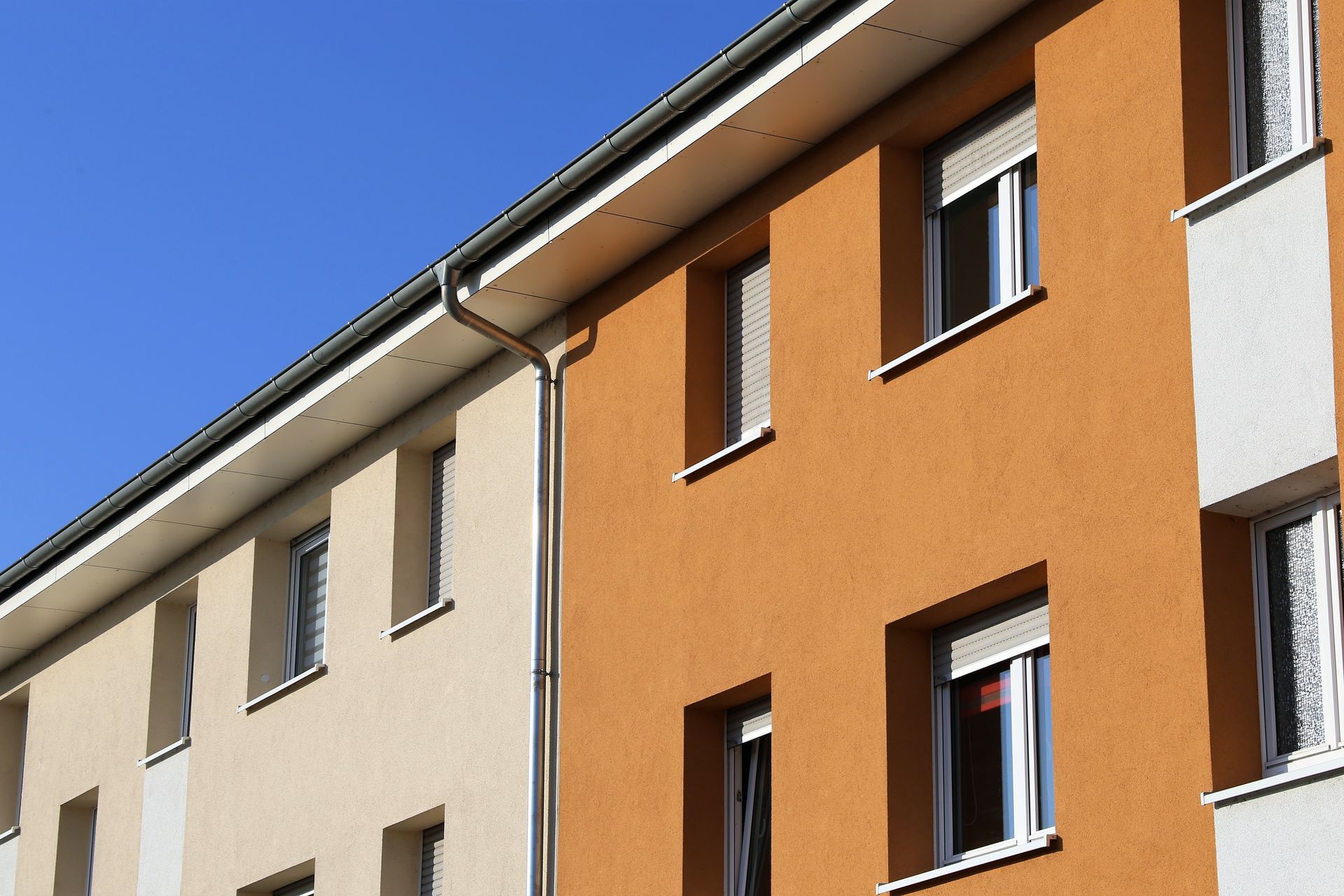 Vue extérieure d'un immeuble à plusieurs étages avec des murs en stuc beige et orange, des encadrements de fenêtres blancs