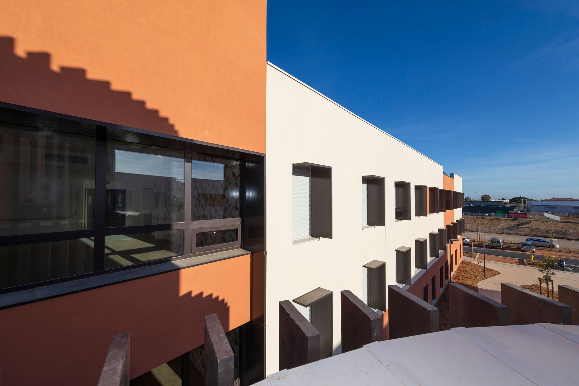 Extérieur d'un bâtiment moderne aux murs orange et blancs, fenêtres sombres et vue sur un ciel bleu