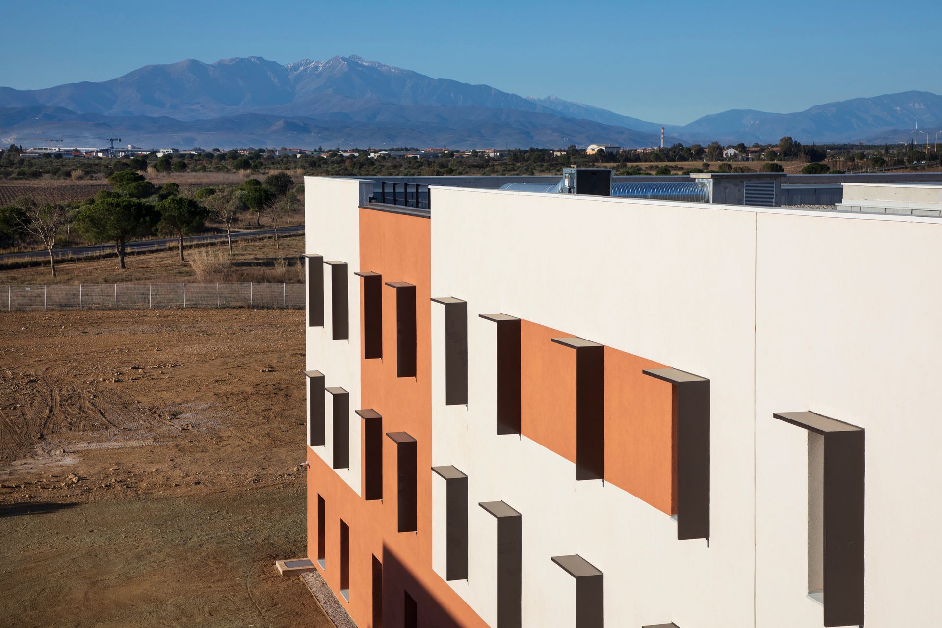Bâtiment moderne blanc et orange dans un paysage aride avec des montagnes à l'horizon