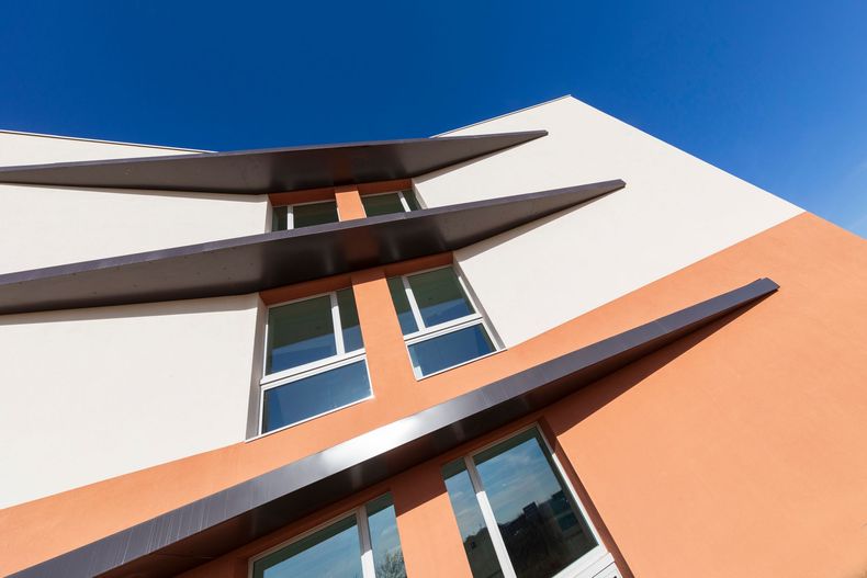Vue en contre-plongée de la façade d'un bâtiment moderne aux murs blancs et orange et aux avant-toits sombres.