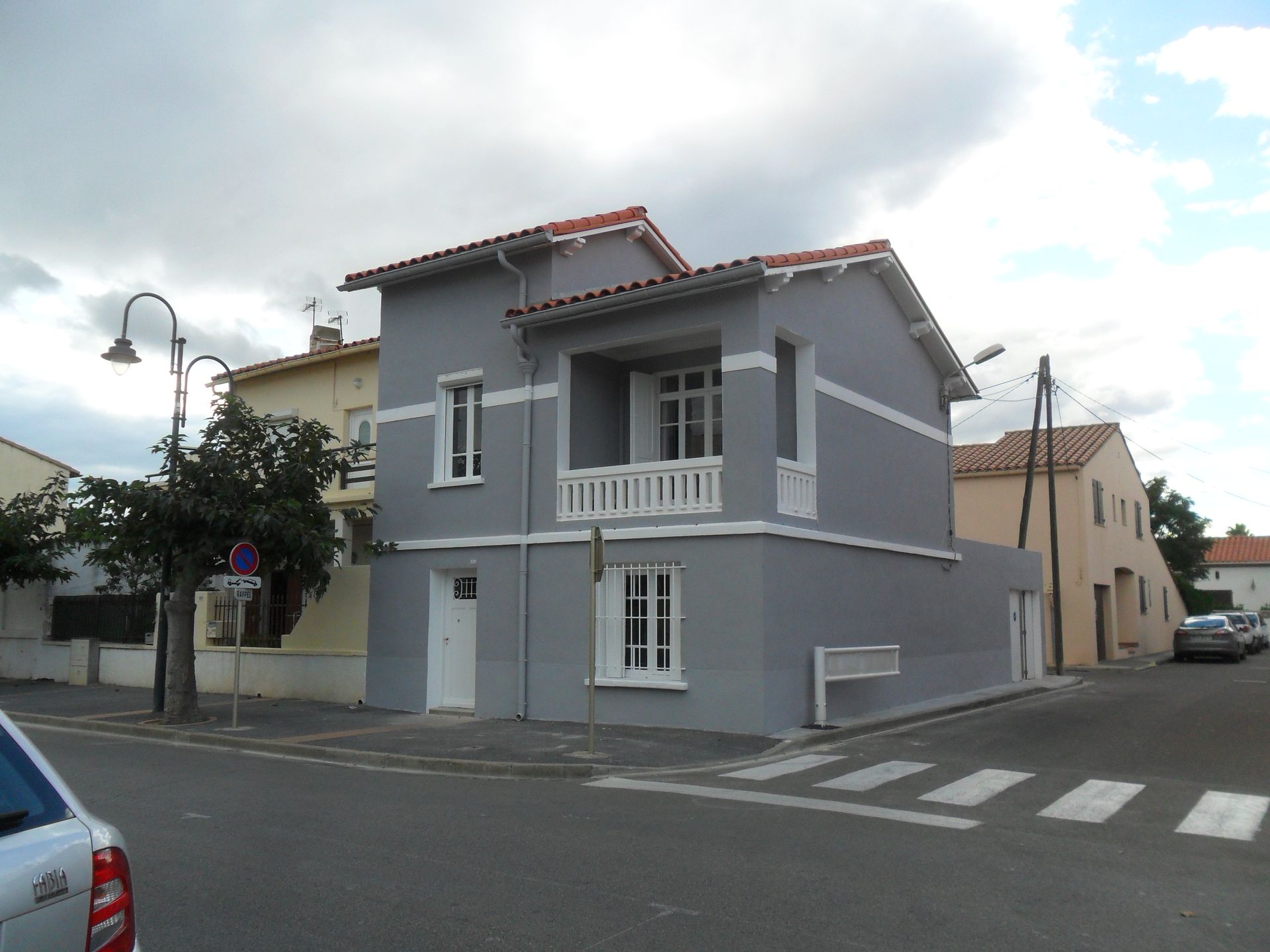 Une maison grise de deux étages avec un balcon et des boiseries blanches