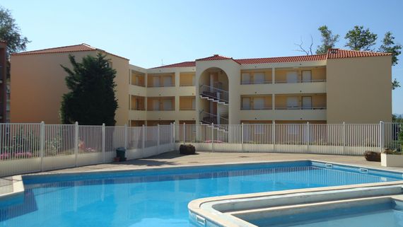 Une résidence de trois étages, à la façade beige et au toit rouge, situé derrière une piscine et une clôture blanche.