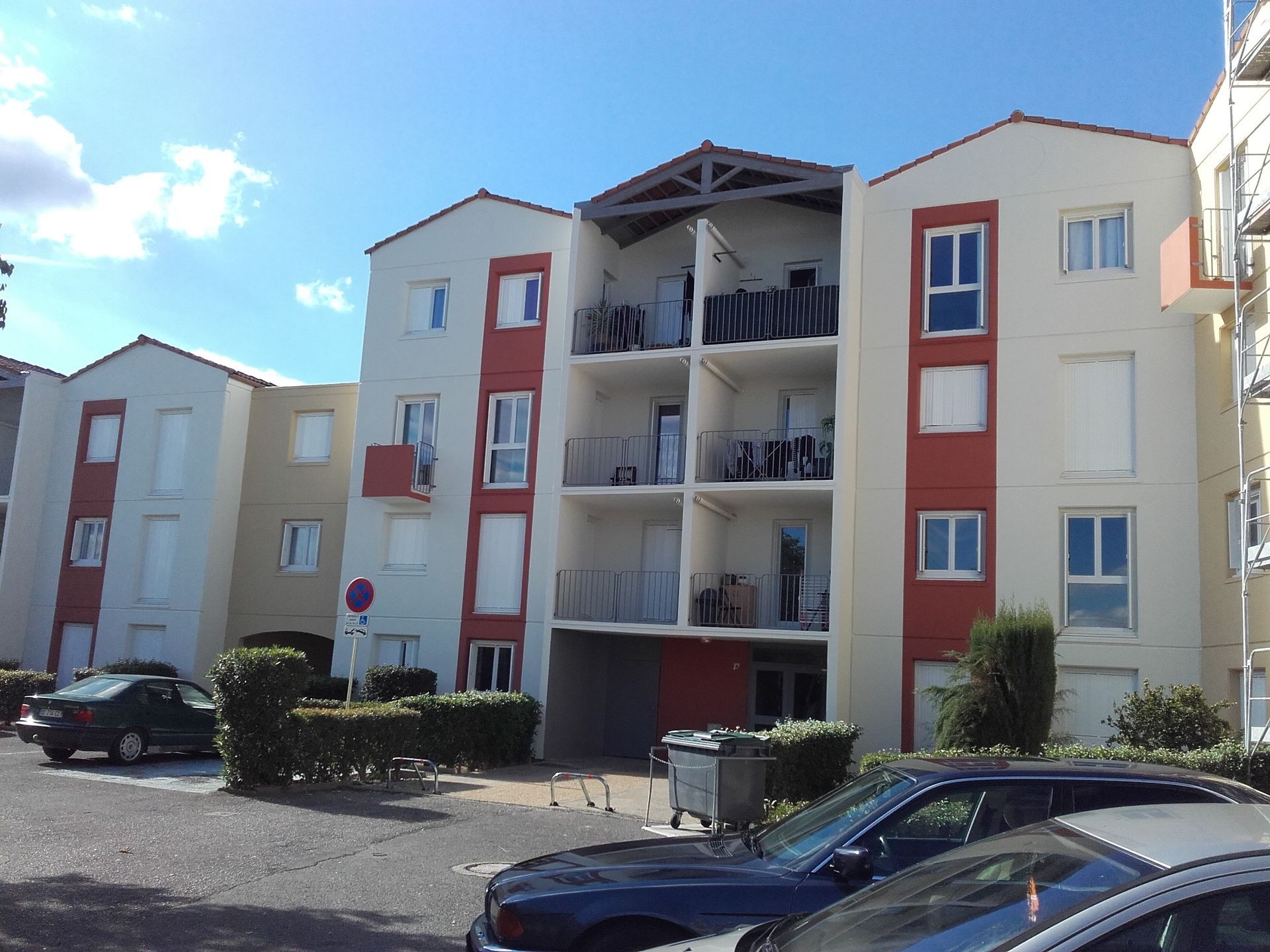 Un immeuble d'appartements de trois étages aux murs beiges, avec des touches de rouge