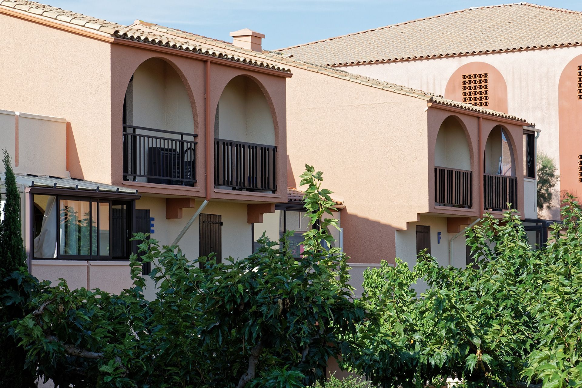 Immeuble d'appartements en stuc rose avec balcons arqués et arbustes verts en façade