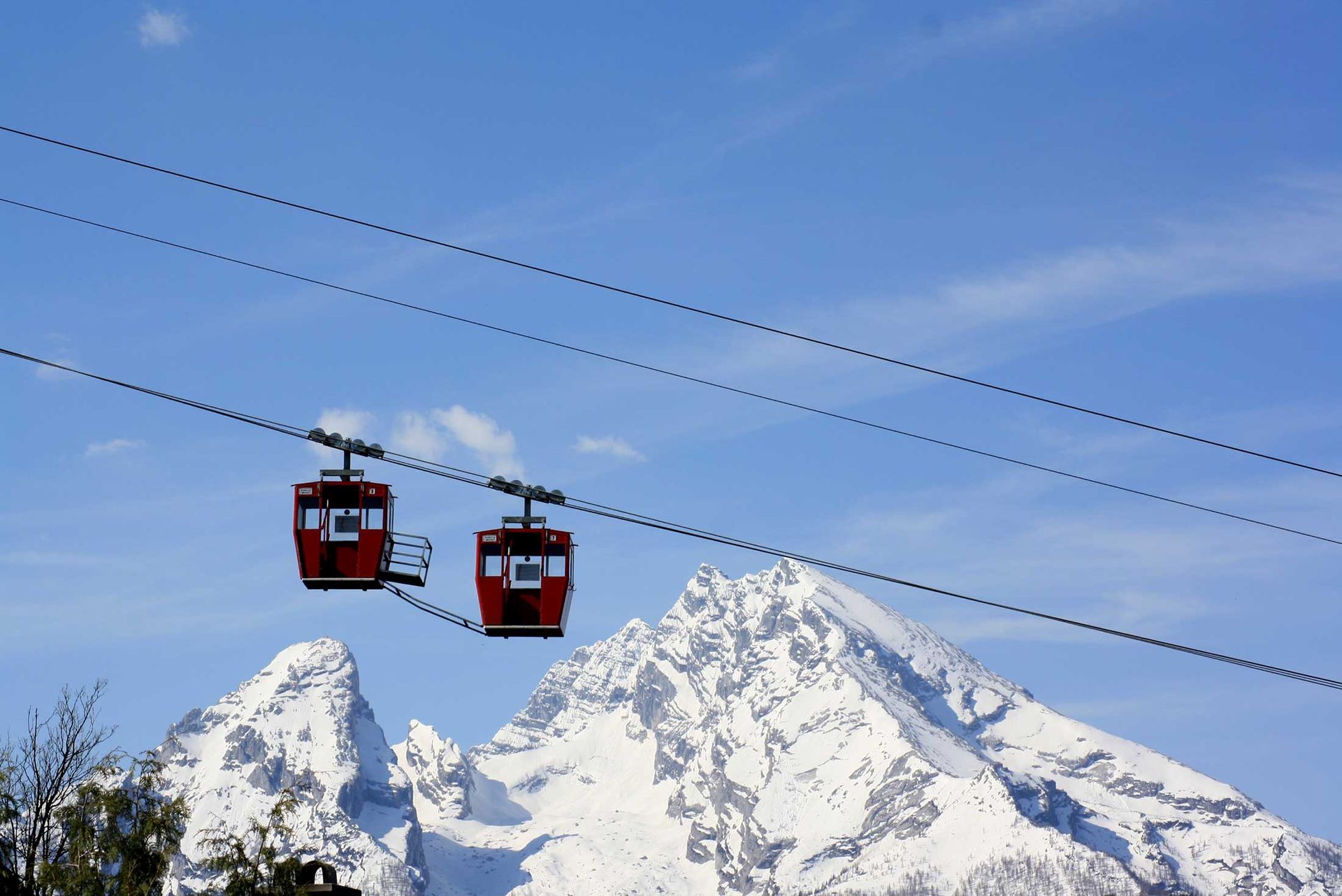 Zwei rote Seilbahnen überqueren schneebedeckte Berggipfel unter einem klaren blauen Himmel