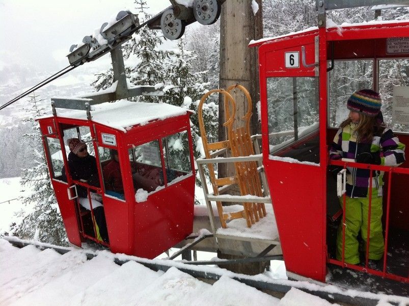 Rote Skiliftkabinen im verschneiten Gebirge, mit zwei dick eingepackten Fahrgästen an Bord.