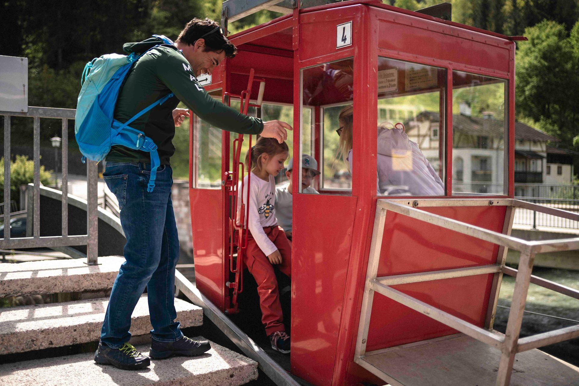 Erwachsener hilft Kind am Bahnsteig in eine rote Seilbahn.