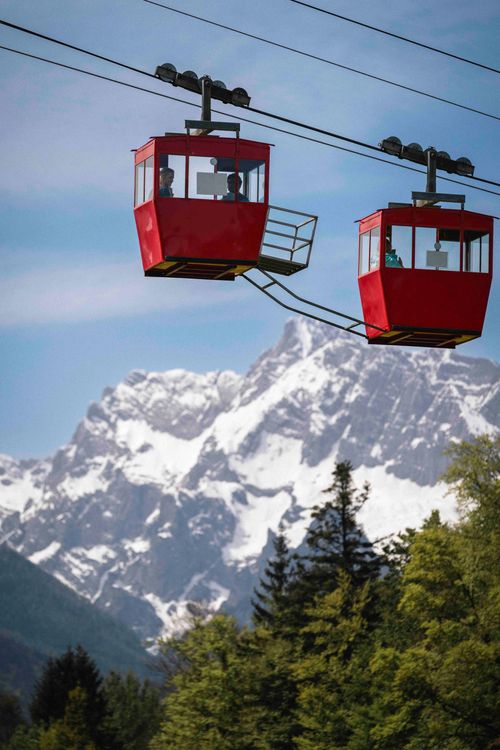 Zwei rote Seilbahnen über einen schneebedeckten Berg mit Bäumen darunter