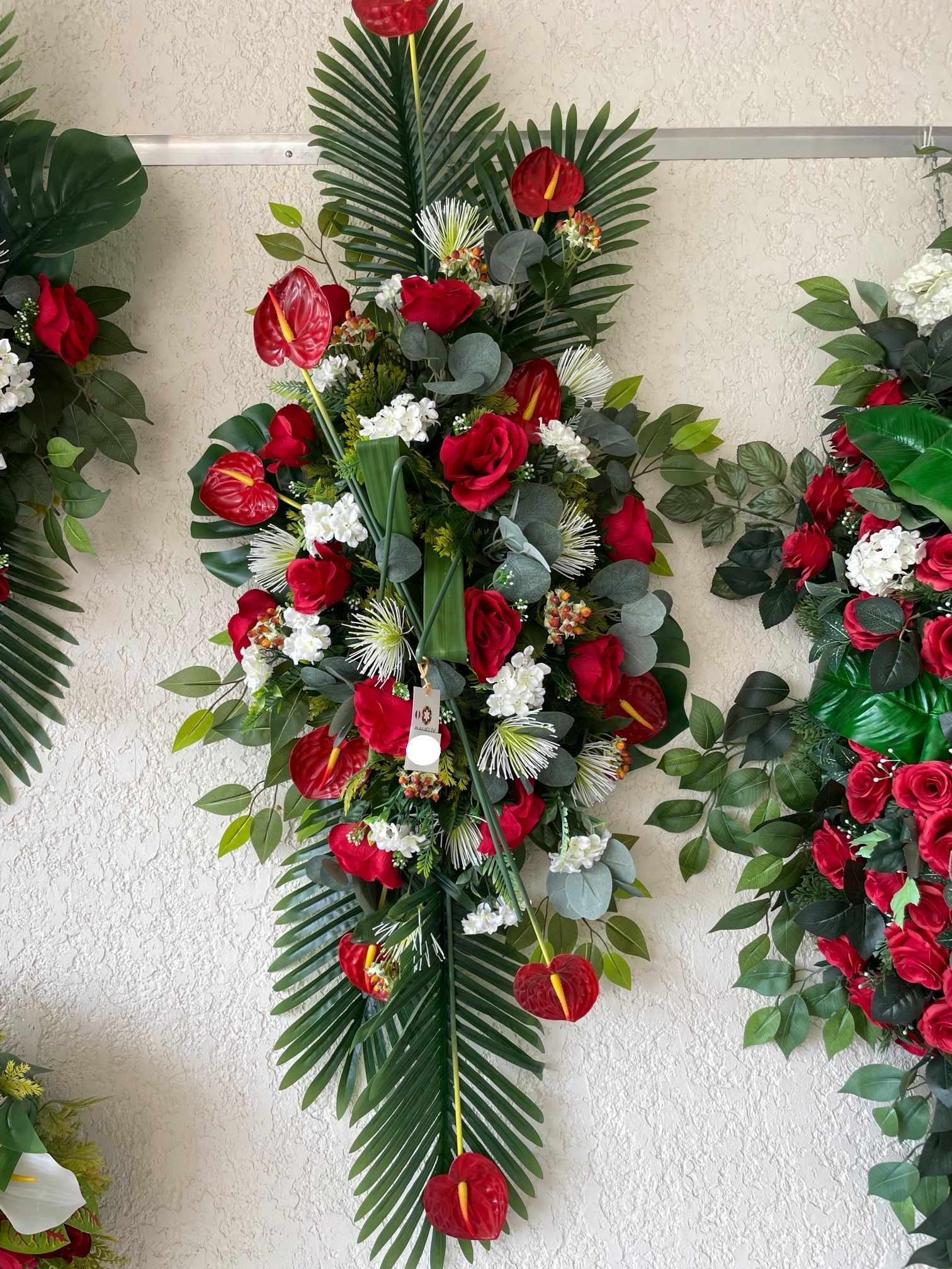 Coussin de fleurs rouges, verts et blanches accroché au mur à côté d'autres coussins