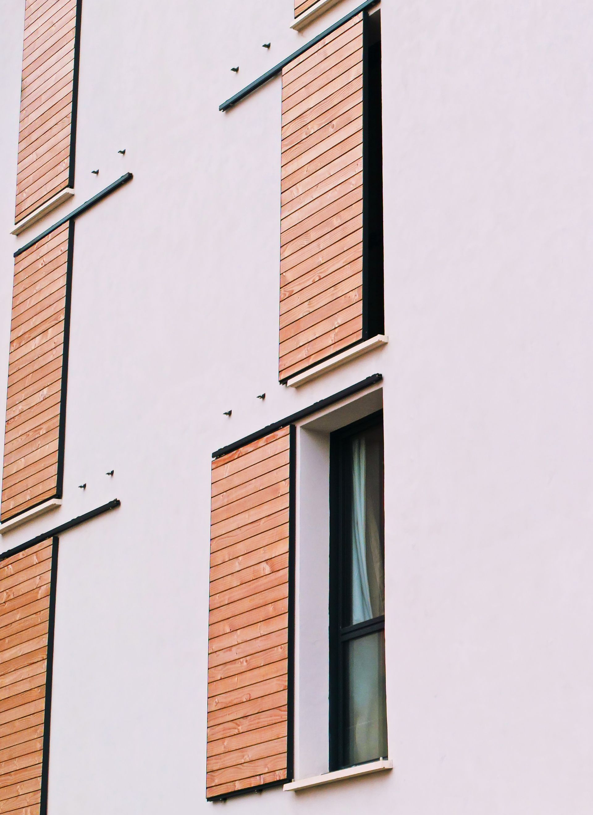 Façade d'appartement moderne avec murs rose pâle, panneaux de briques orange et fenêtres verticales étroites.