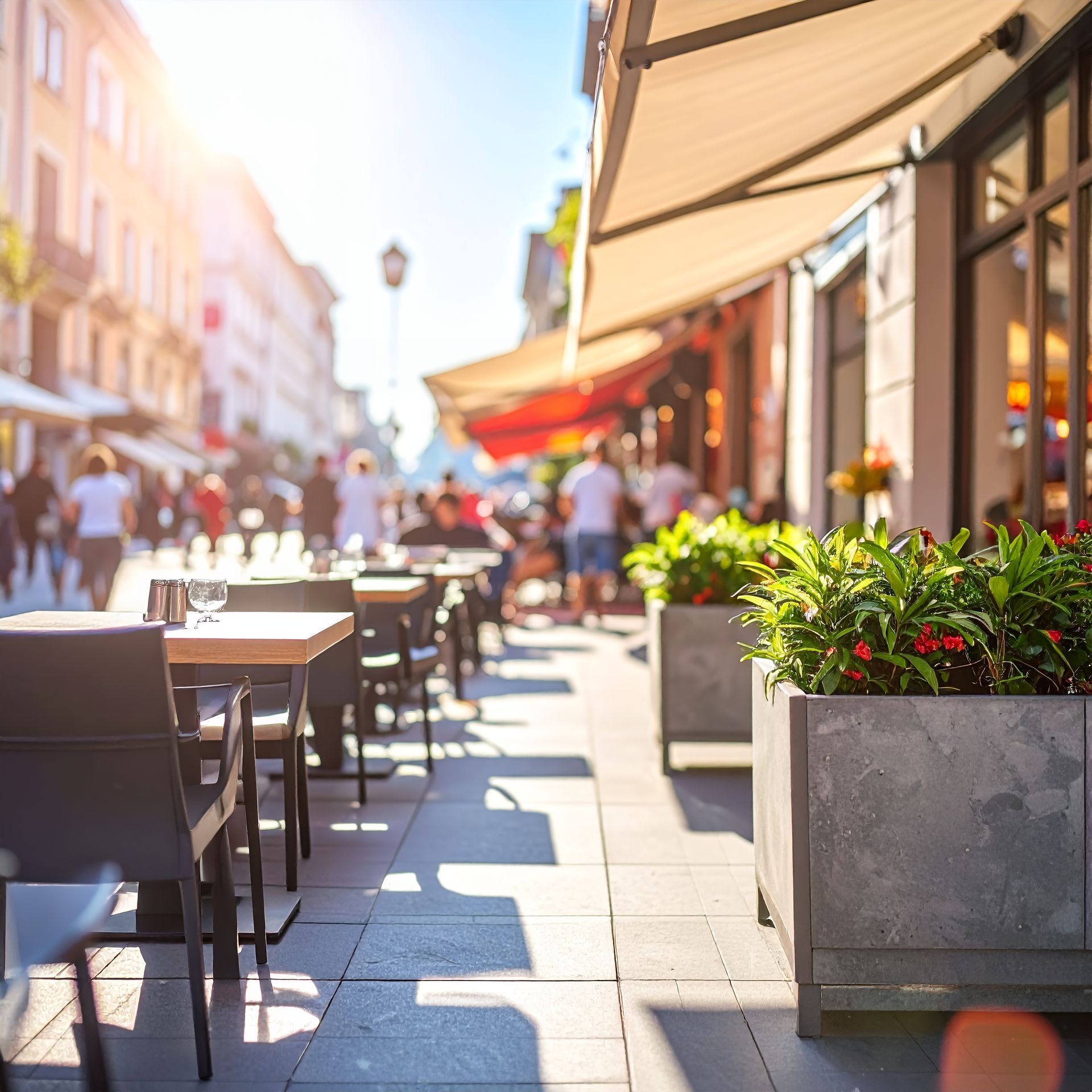 Terrasse ensoleillée d'un café avec tables, chaises et pots de fleurs vides, le long d'une rue de la ville.