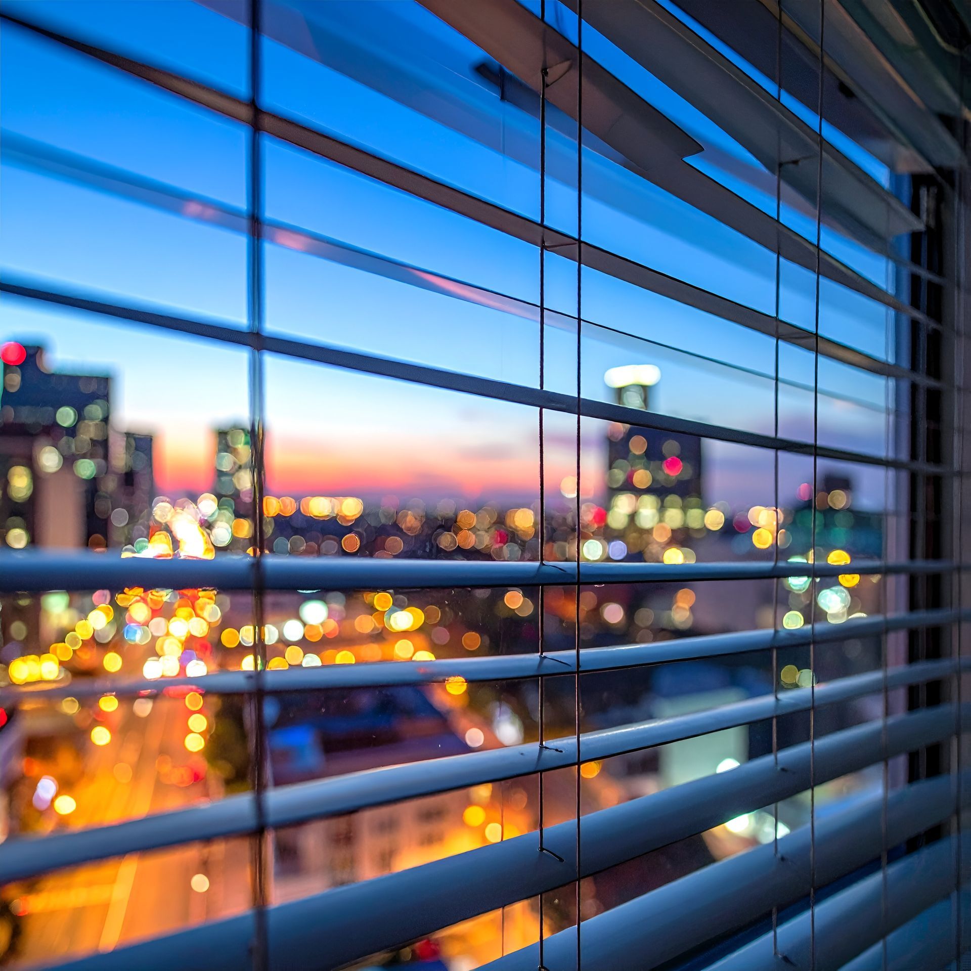 Lumières de la ville aperçues à travers les stores bleus au crépuscule.