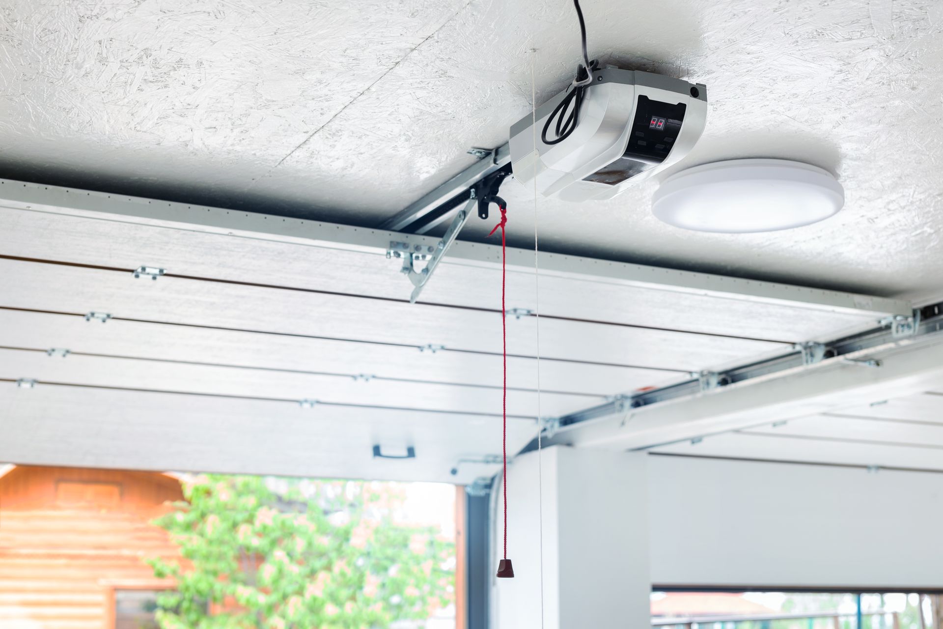 Ouvre-porte de garage fixé au plafond avec un cordon rouge.