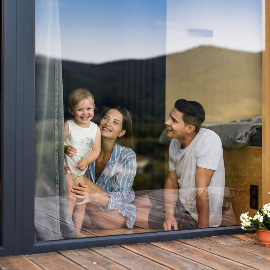 Une famille souriant près d'une fenêtre, avec un enfant sur les genoux d'une femme et un homme à côté d'eux.