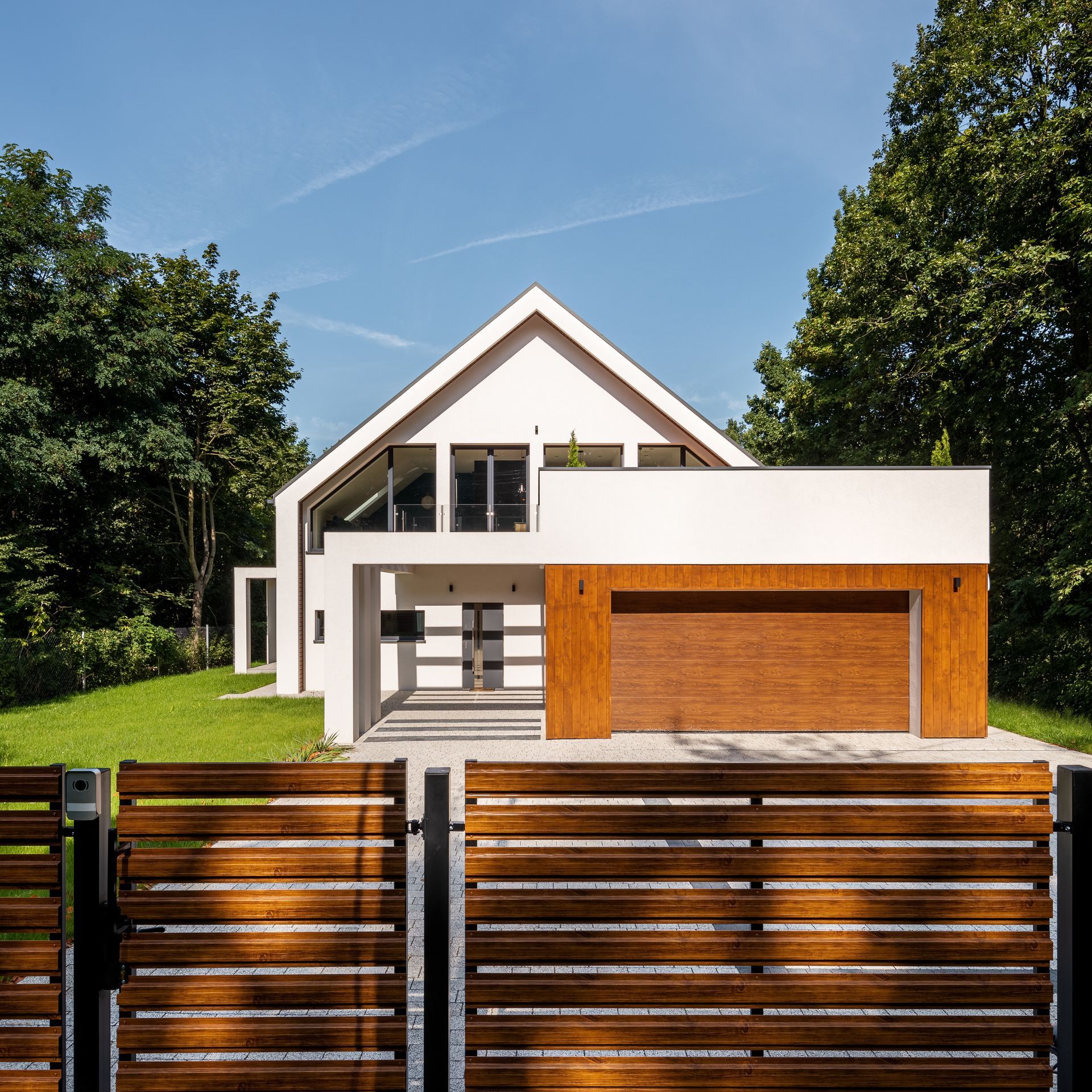 Maison blanche moderne avec garage en bois et portail d'entrée donnant sur une pelouse verdoyante et ensoleillée.