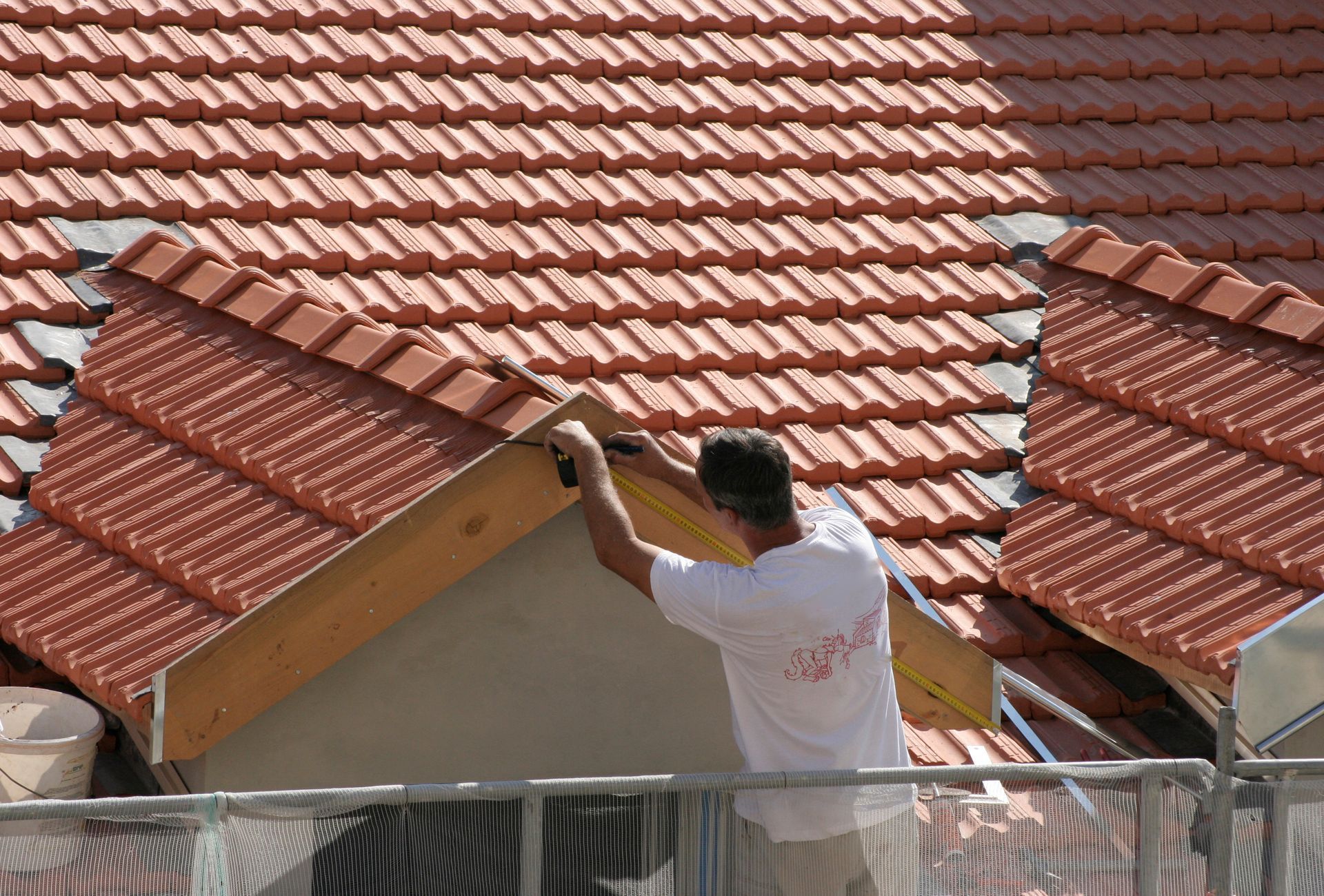 Couvreur par une journée ensoleillée travaillant sur une toiture en tuiles en terre cuite, à l'aide d'un outil sur un support en bois.