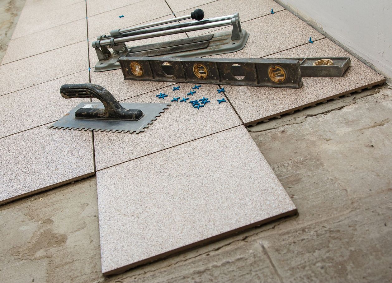 Pose de carrelage en cours : coupe-carreaux, niveau, truelle et carreaux sur une surface en ciment.