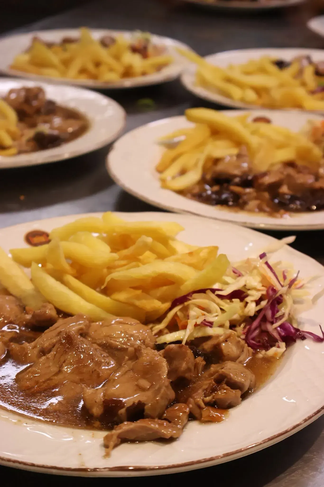 Platos de estofado sabroso, patatas fritas doradas y una guarnición de ensalada de col rallada dispuestos sobre una mesa.