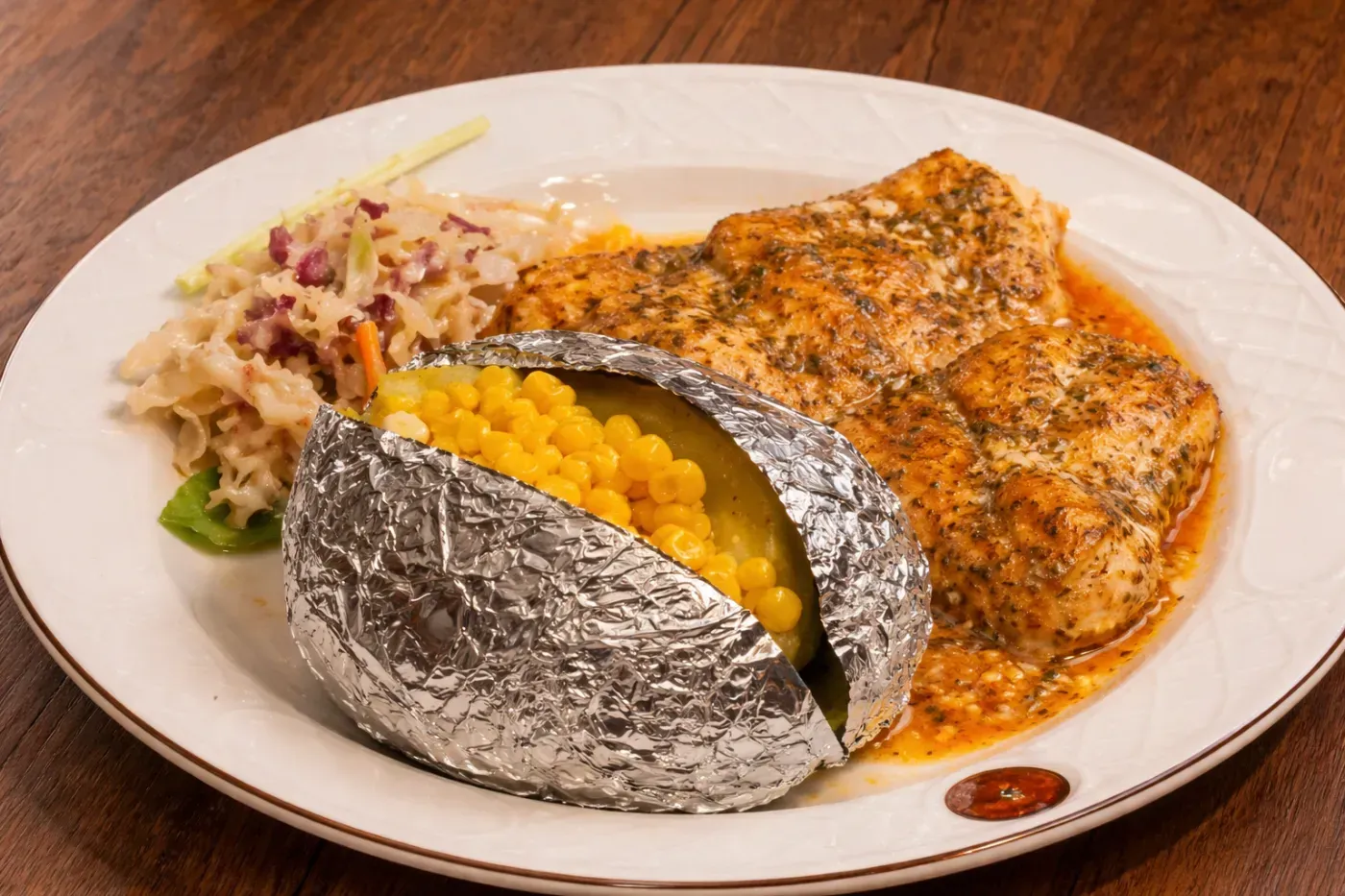 Two baked potatoes, one open with corn, beside a seasoned grilled fish fillet on a white plate