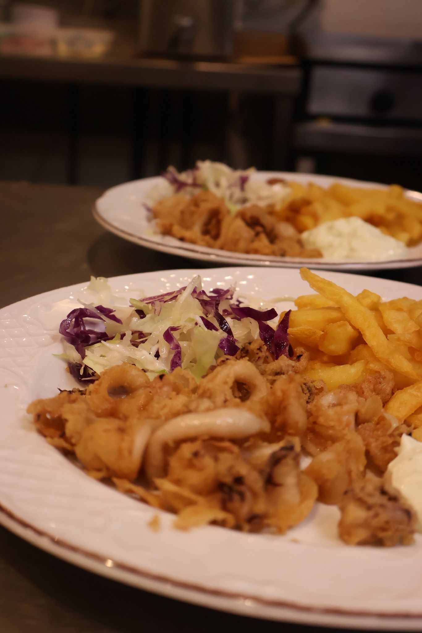 Platos de mariscos fritos con papas fritas y ensalada de col morada en la mesa de un restaurante.