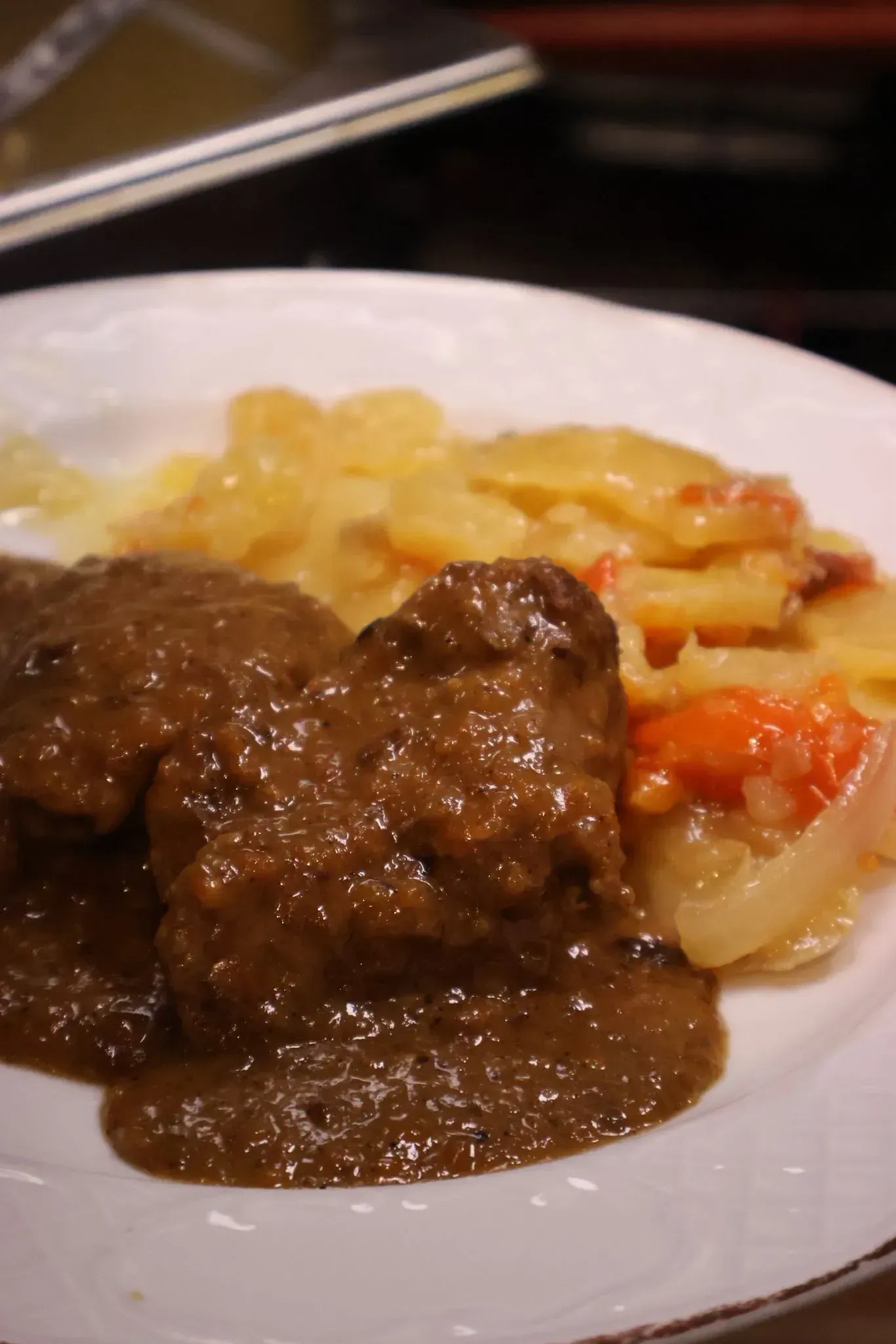 Plato con carne en salsa marrón, patatas y verduras mixtas en un plato blanco.