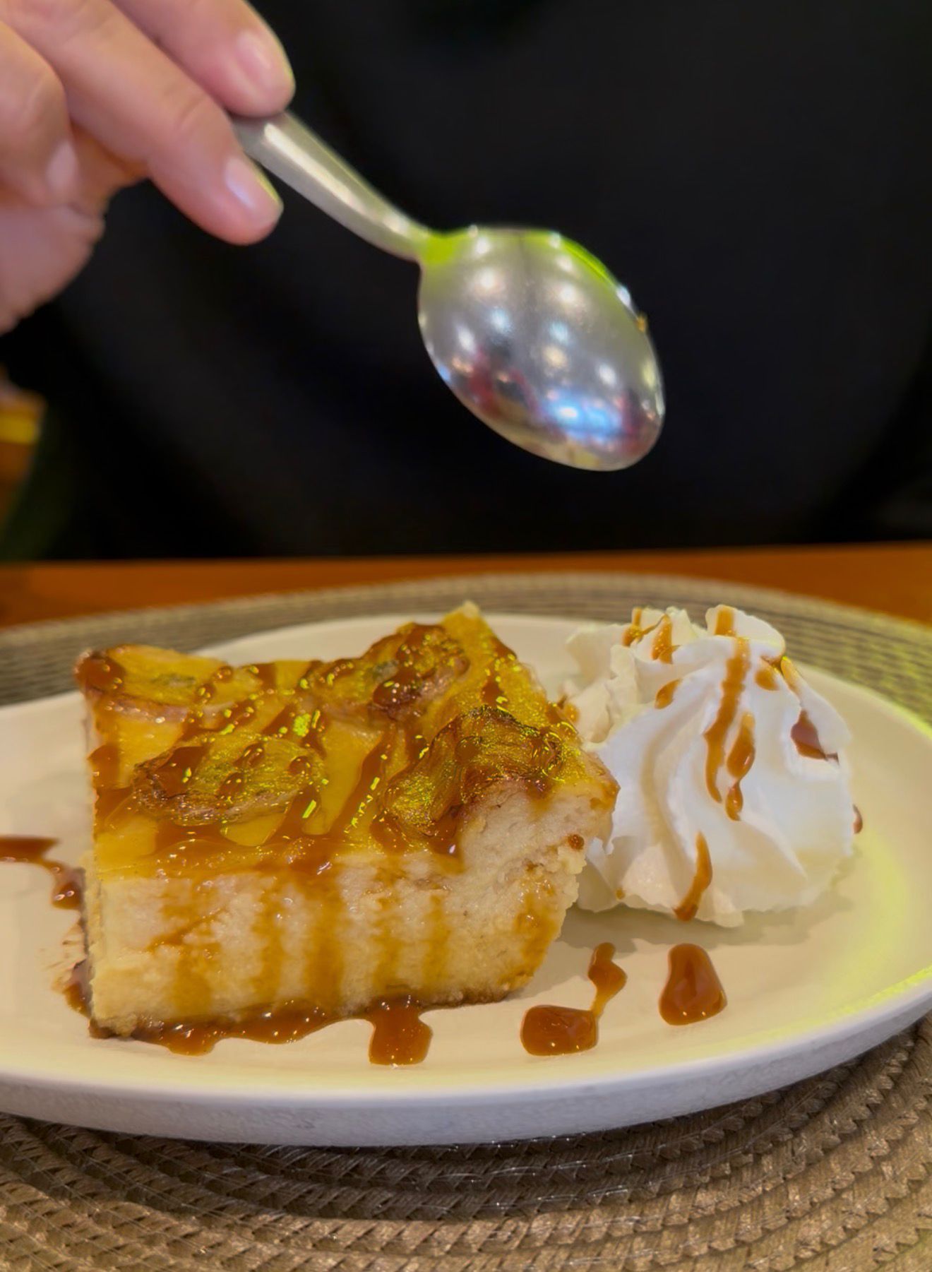 Plato de postre con bizcocho bañado en caramelo y nata montada, mientras una cuchara se cierne sobre él.