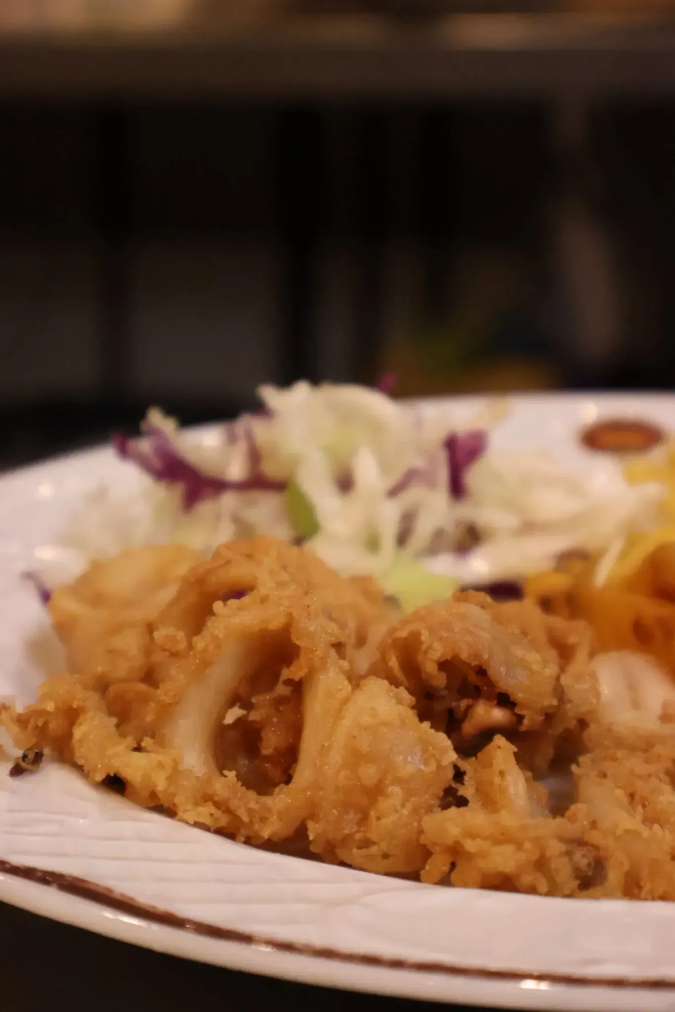 Anillos de calamar fritos, crujientes y dorados, servidos en un plato blanco con una guarnición de ensalada de col.