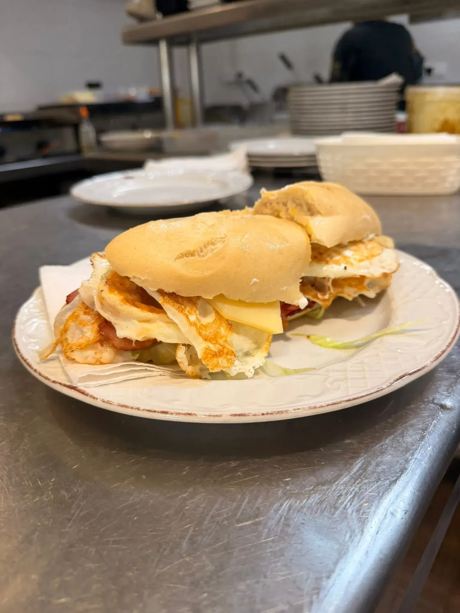 Sándwich en un plato blanco sobre una encimera de acero inoxidable en un entorno de cocina.