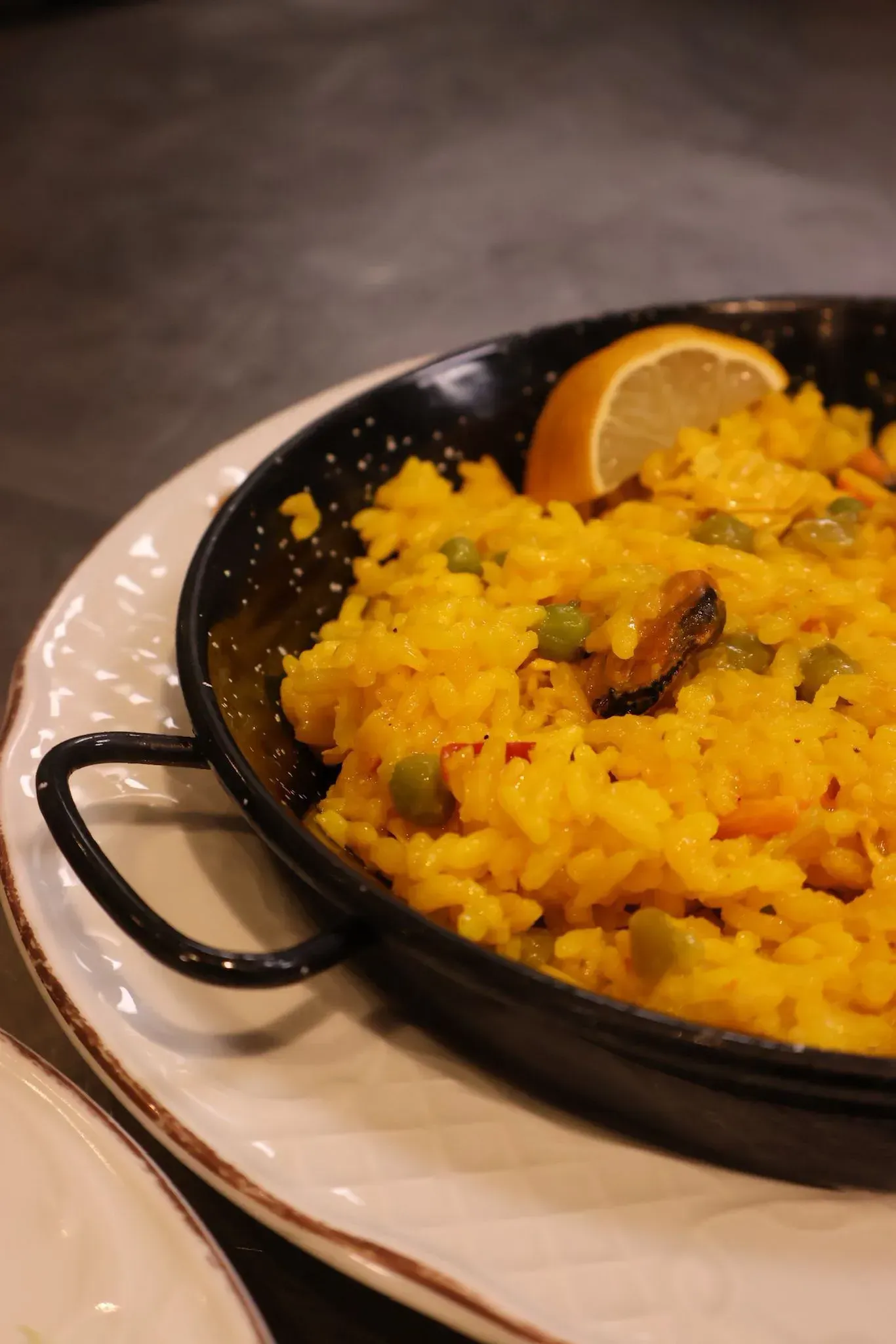 Arroz amarillo en una sartén negra sobre un plato blanco, coronado con una rodaja de limón.