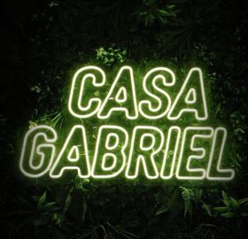 Glowing neon sign reading &ldquo;CASA GABRIEL&rdquo; against a dark leafy background