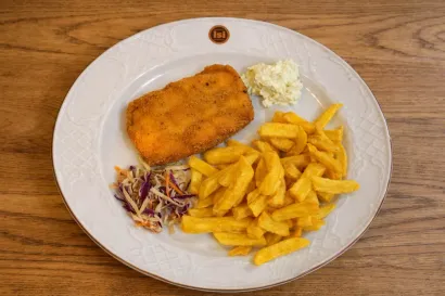 Un filete de pescado frito servido con patatas fritas doradas, ensalada de col y salsa tártara en un plato blanco.
