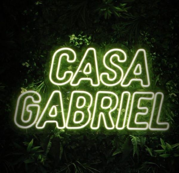Glowing neon sign reading &ldquo;CASA GABRIEL&rdquo; against a dark leafy background